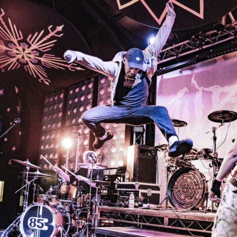 Singer jumping in front of the drum kit at Club 85